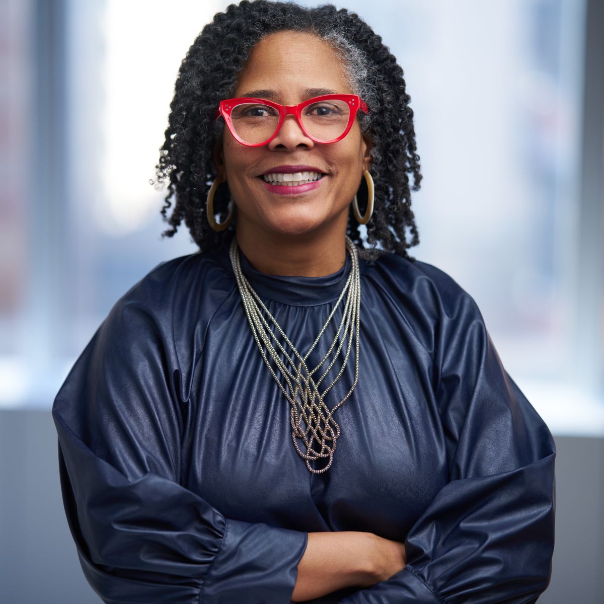 Professional woman with red glasses and black blazer smiling with arms crossed